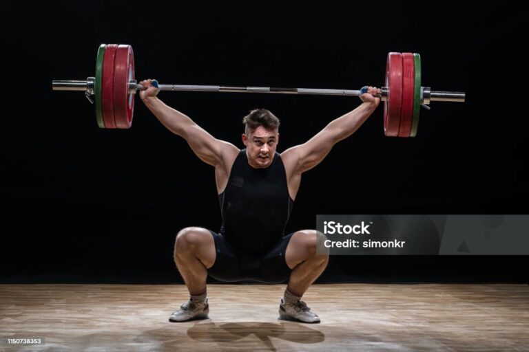 Young man lifting barbell against black background.